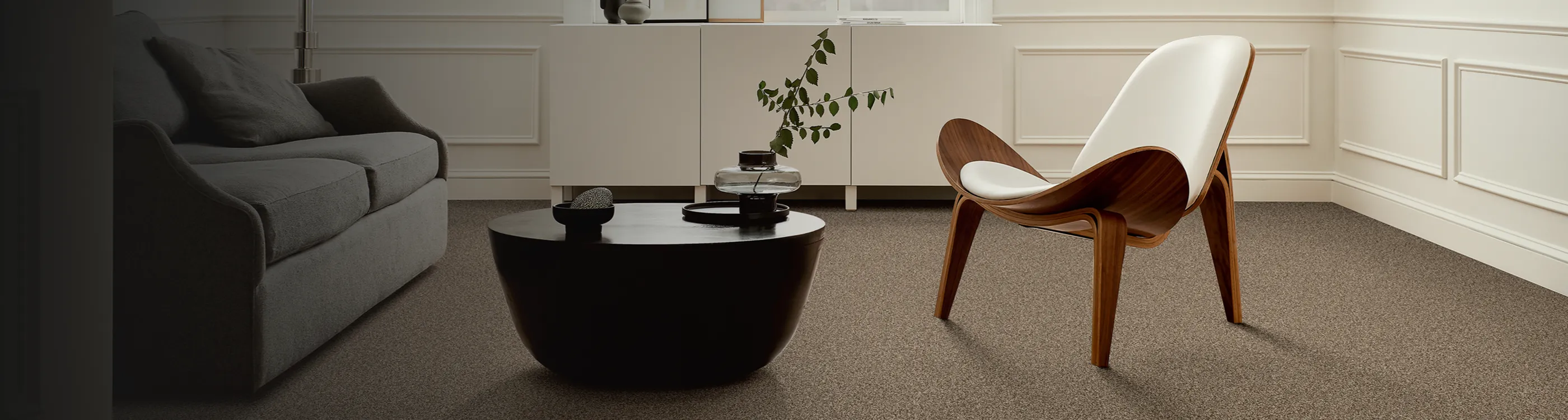 beige carpeted floors in contemporary modern living room with white chair, black coffee table and abstract art